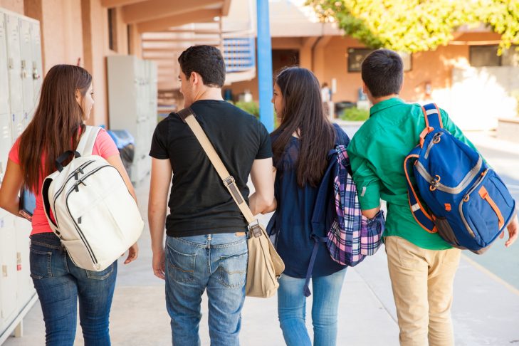 Four students wearing backpacks walking side by side at school